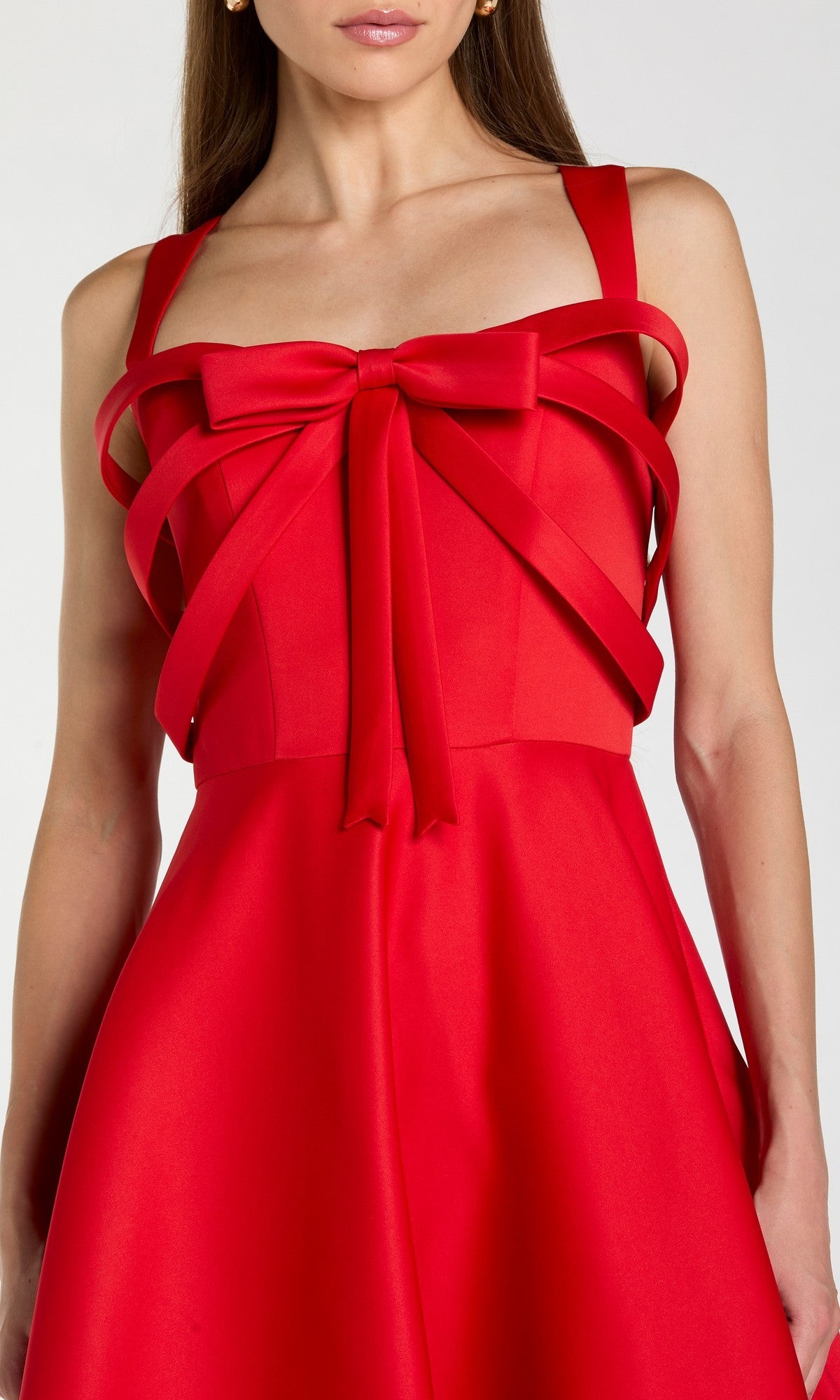 A woman wears the Tea-Length Party Dress: Mac Duggal 21247—a sleeveless red satin cocktail dress with a striking bow detail on the chest. The fitted bodice and flared waist create an elegant, timeless silhouette.